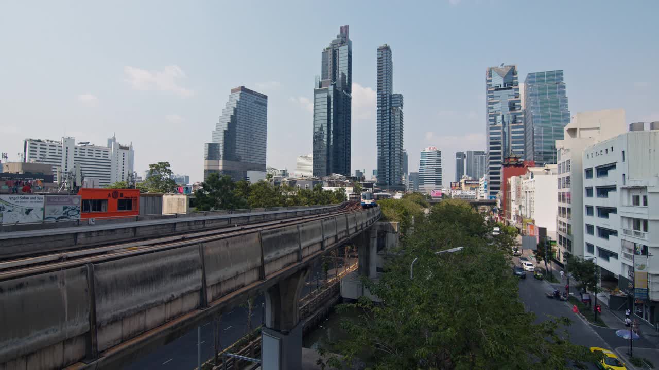火车行驶在熙熙攘攘的街道上，林立着高耸的摩天大楼。曼谷泰国视频下载