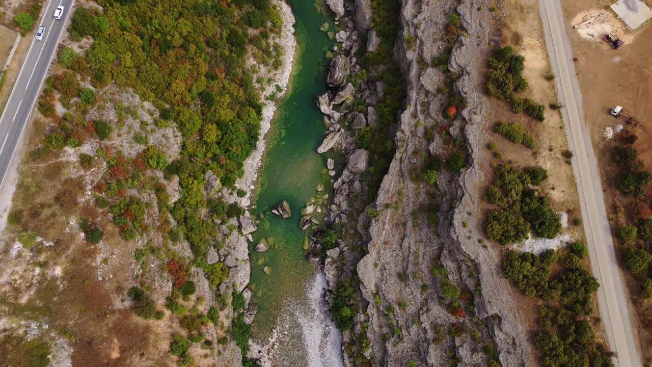 无人机俯瞰风景如画的岩石峡谷与翡翠水莫拉卡河，柏油路与移动的汽车和人行道，黑山。充满活力的绿色植被在夏天。热门旅游目的地视频素材