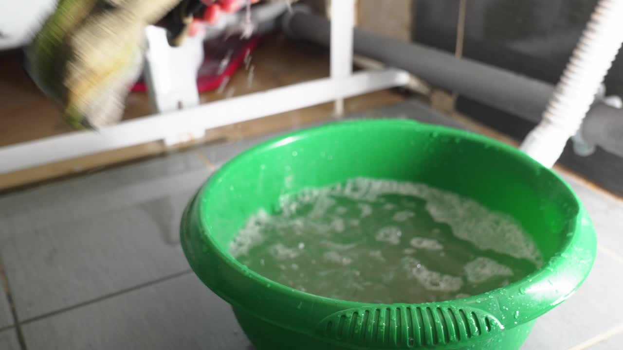 由于浴室漏水，一名男子用抹布在桶里收集水。视频素材
