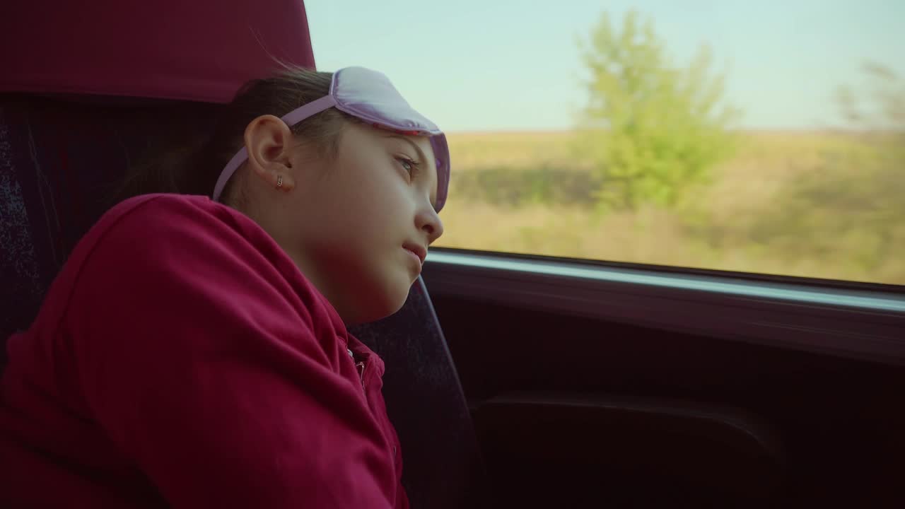 关闭了。小女孩在火车上厌倦了旅行，把它戴在眼睛上，在旅途中靠在窗户上休息。来自乌克兰的难民。疲惫的孩子在运输车辆上用眼罩遮挡阳光视频素材