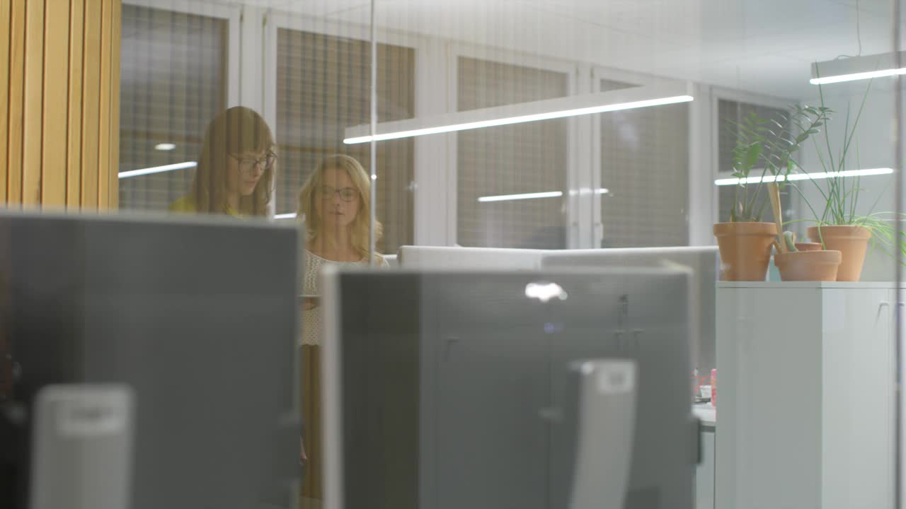 两名女同事在办公室走廊上讨论着视频下载