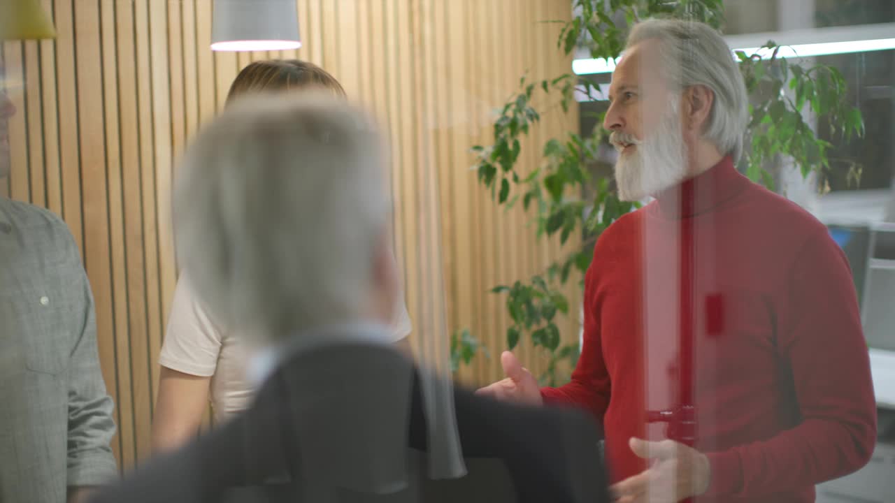 一个灰胡子男人在玻璃会议室里跟人说话视频下载