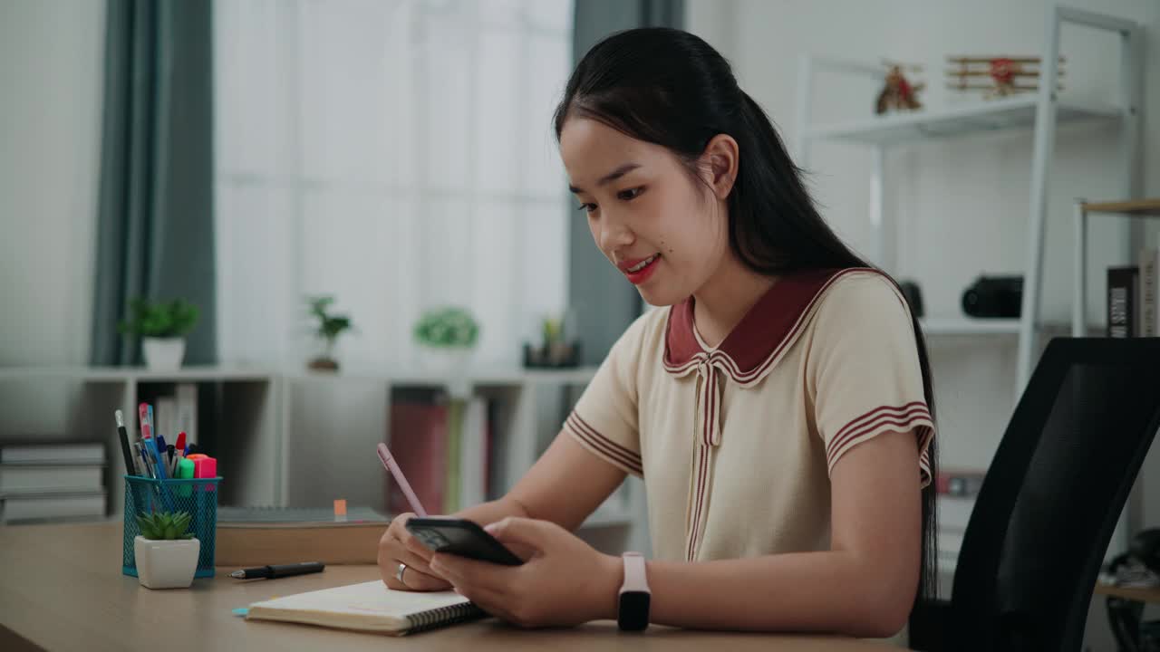 快乐的年轻亚洲女子坐在书桌前，用绿色记号笔在日记中标出重要的事情。视频素材