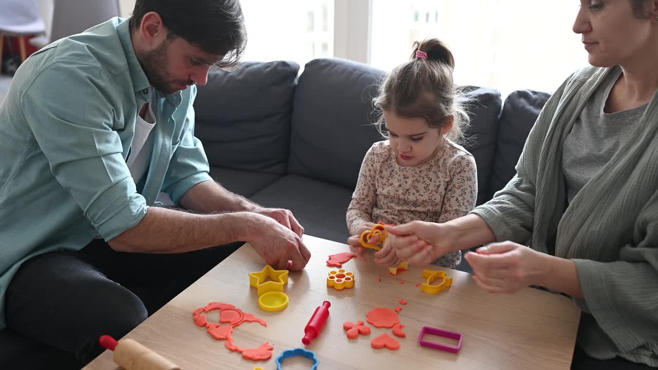 父母和女儿在家里玩粘土。一个小女孩正在用橡皮泥做造型的家庭视频下载