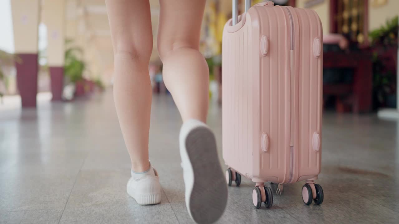 一个人，很可能是一个女人，在一个旅游终端站带着一个滚动的手提箱走着，这意味着一次旅行。视频下载