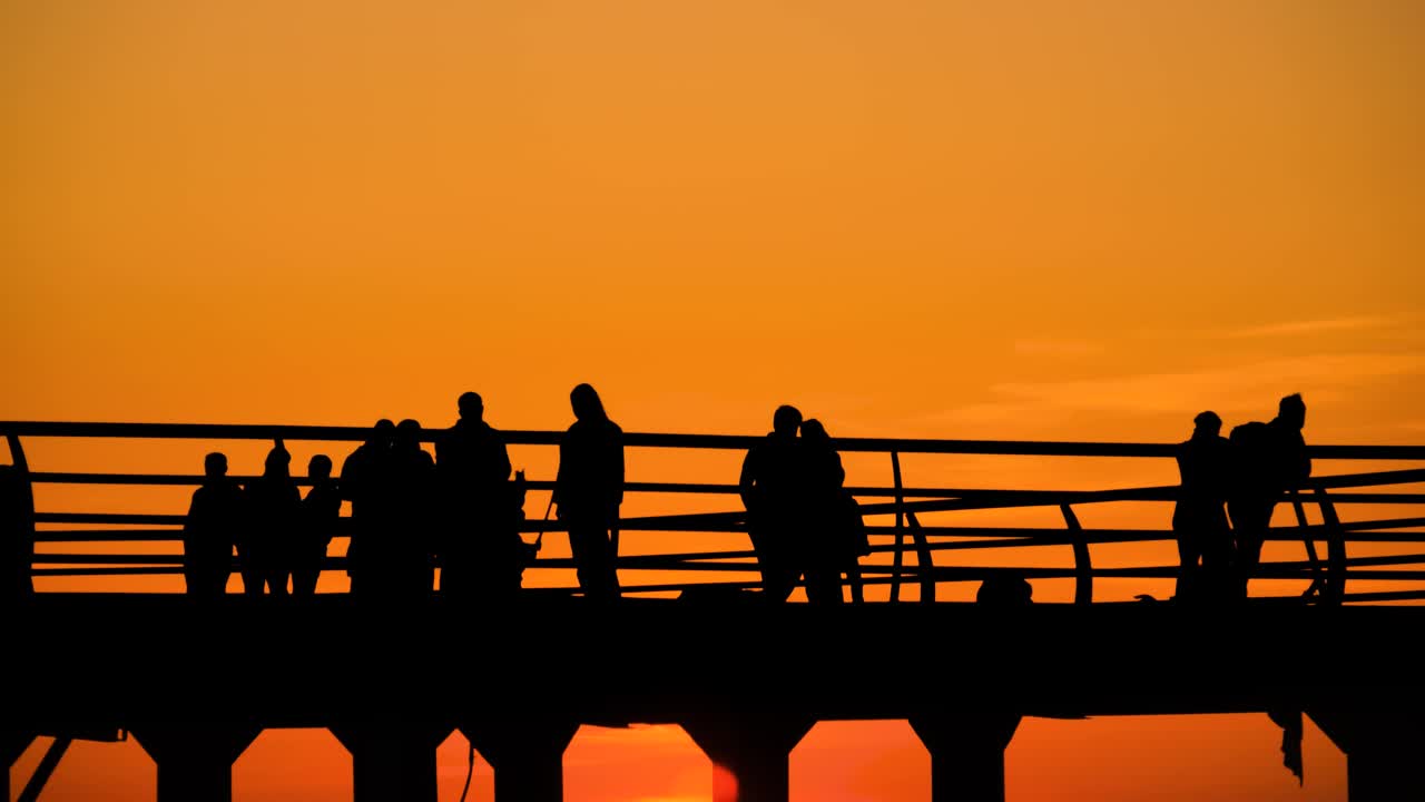 橘黄色的晚霞映衬着码头上行人的剪影视频素材