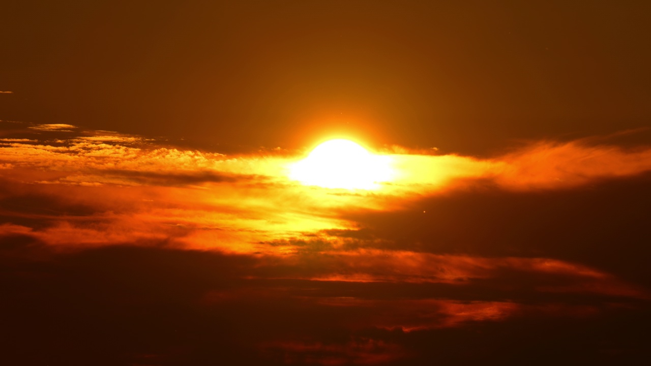 太阳落在橙黄红色的天空中，描绘了一幅史诗般的景象，太阳像明亮而炽热的圆盘。鲜艳的太阳躲在电影般的云彩里，美丽的夏日天空，黄金时刻。视频下载