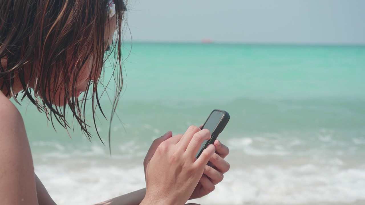 亚洲女性在海滩上使用智能手机。视频下载