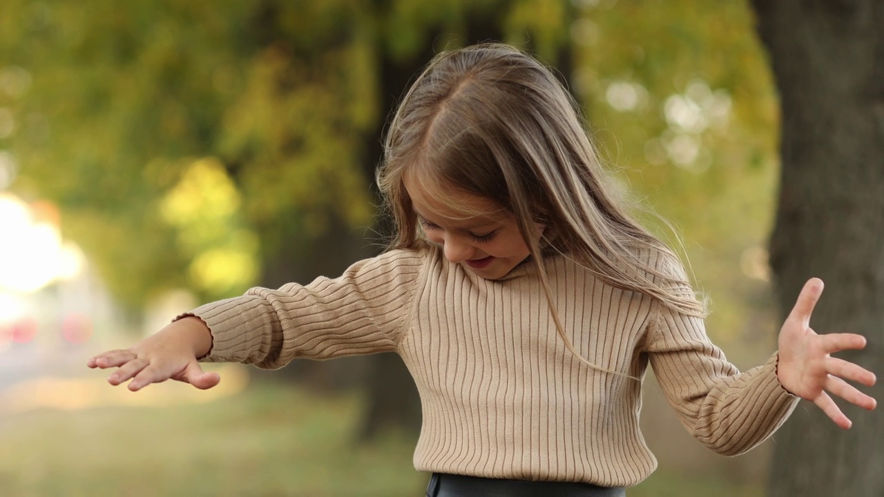 儿童节。5-6岁的开朗的小女孩在秋天的公园里笑着玩落叶。白人学龄前儿童穿着针织毛衣。秋季假期的休闲活动。视频下载