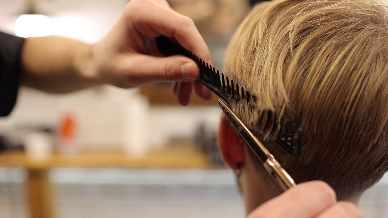 理发师用专业的剪刀和梳子在理发店里剪男人的金发。美发师在沙龙创造现代男性发型。风格与职业理念视频下载