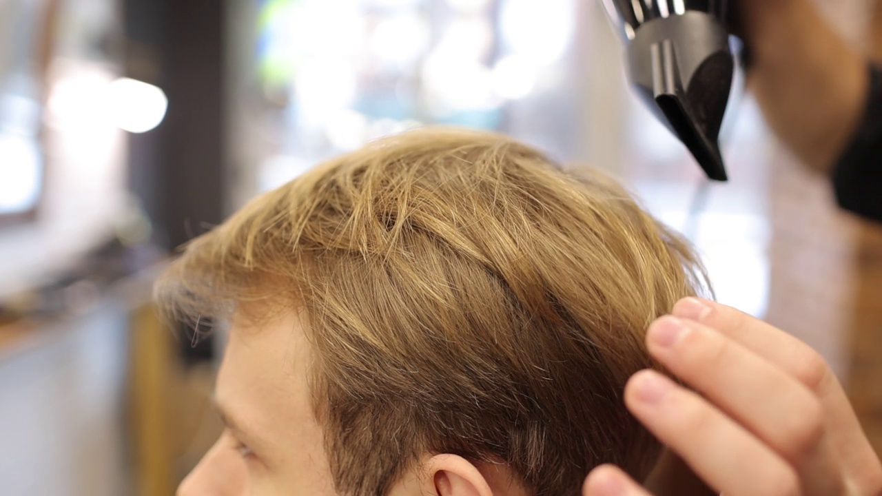 专业理发师在理发店用吹风机和梳子吹干男士的金发。美发师在沙龙创造现代男性发型。客户服务。美丽的概念视频下载