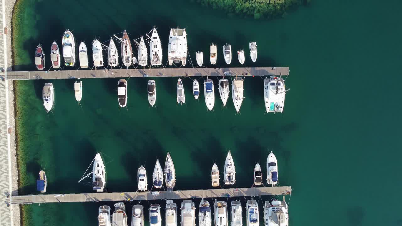 在木制码头附近的游艇俱乐部里，豪华帆船和船只的鸟瞰图。欧洲城市的俯视图。停泊在海岸附近的大型船只。通往灯塔的路。夏季游艇概念。视频下载