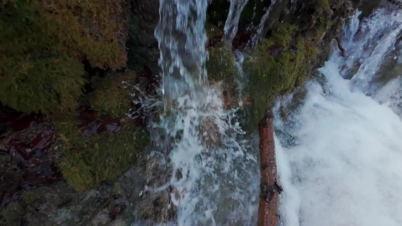 山间的一条小溪流，活灵活现，水花四溅。新鲜的泉水在长满苔藓和白雪覆盖的岩石间流淌。缓慢的运动。视频下载