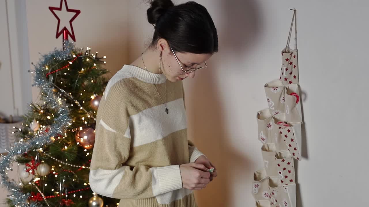 一个十几岁的女孩从降临节日历中拿出一份圣诞惊喜礼物。视频下载