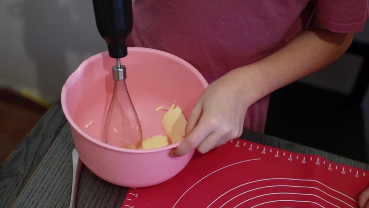 一个女孩用搅拌器在碗里搅拌黄油。视频下载