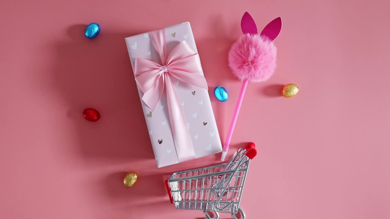 礼品盒，巧克力复活节彩蛋和粉红色背景的购物车。视频下载