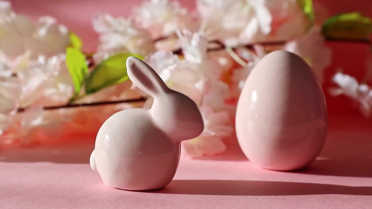 瓷复活节兔子和鸡蛋与一个苹果树枝在粉红色的背景。视频下载