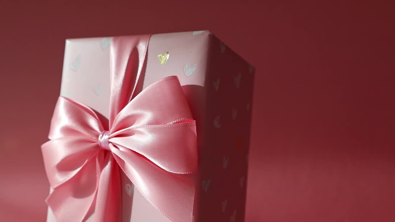一个礼盒，粉红色背景上有蝴蝶结。视频下载
