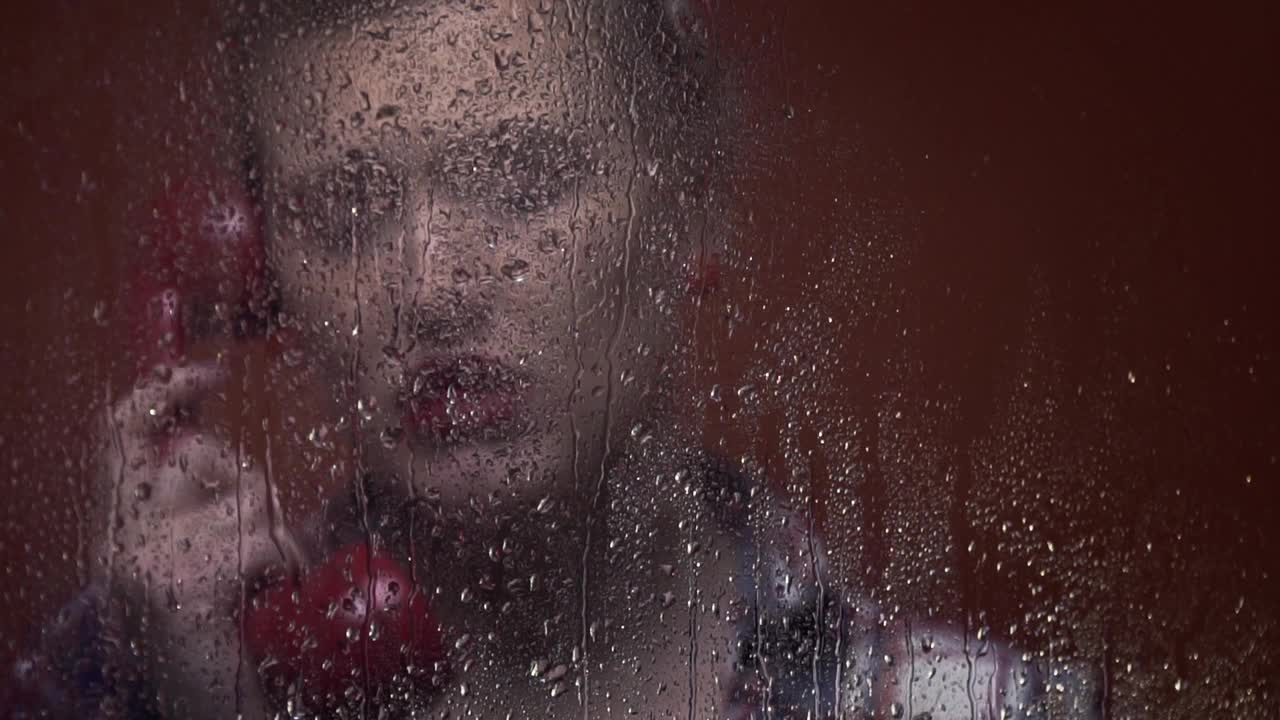 一个有着迷人复古发型的金发女人正站在被雨淋湿的窗户后面讲电话视频下载