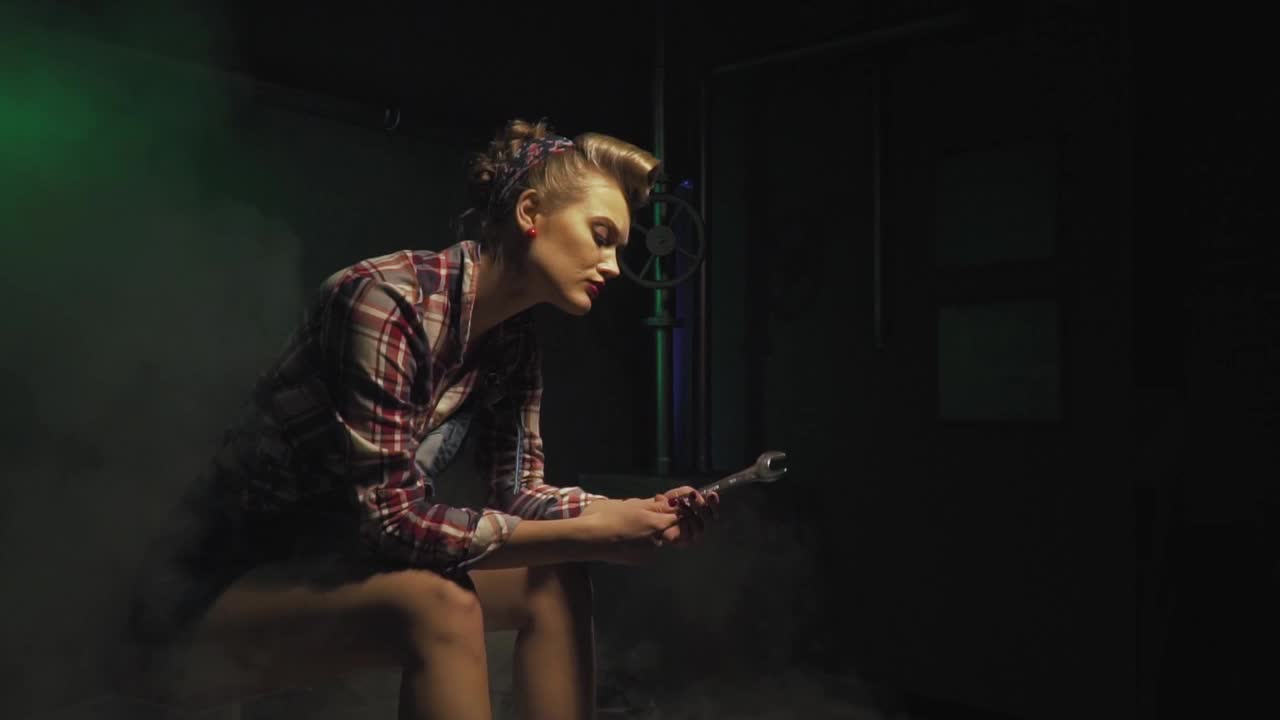 穿着牛仔裤短裤的女机械师拿着扳手坐在一个充满蒸汽的房间里视频素材
