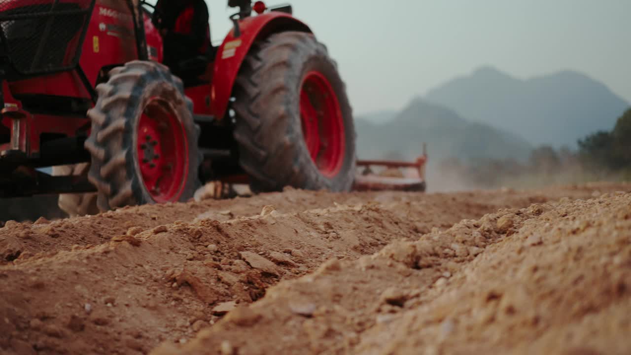 亚洲农民开着红色拖拉机在耕地上翻耕，翻出耕地中的泥土和作物残渣。2024年1月29日，在泰国清莱，准备种植玉米视频下载
