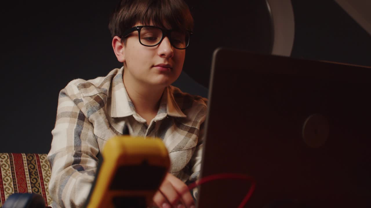 戴眼镜的可爱少年戴上耳机，开始在笔记本电脑上愉快地聊天。青少年活动及爱好视频下载