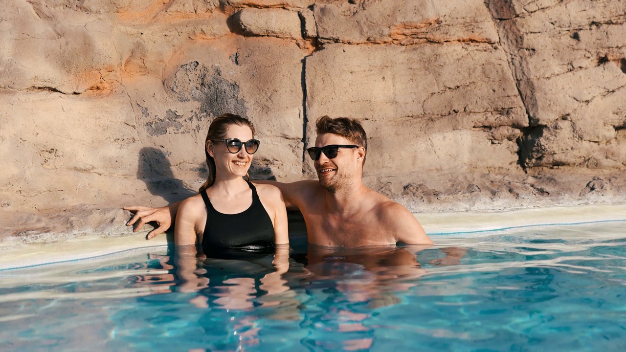 微笑的情侣一起在温泉泳池放松。浪漫的度假视频下载