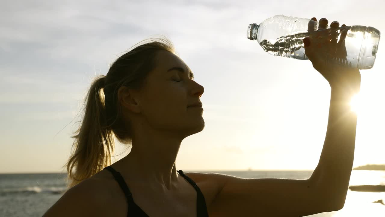 运动的女人在户外健身训练后从瓶子里倒清爽的水在脸上视频下载