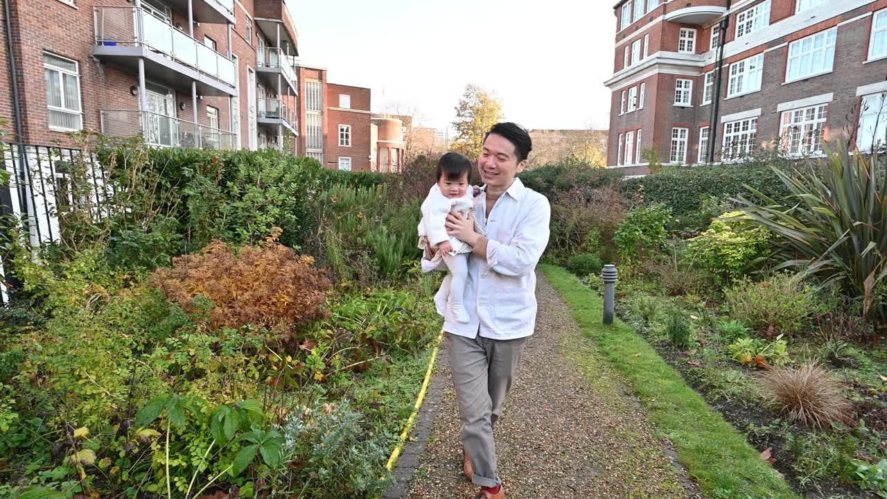 亚洲家庭带着孩子在公园散步，父亲抱着孩子，享受阳光明媚的日子视频素材
