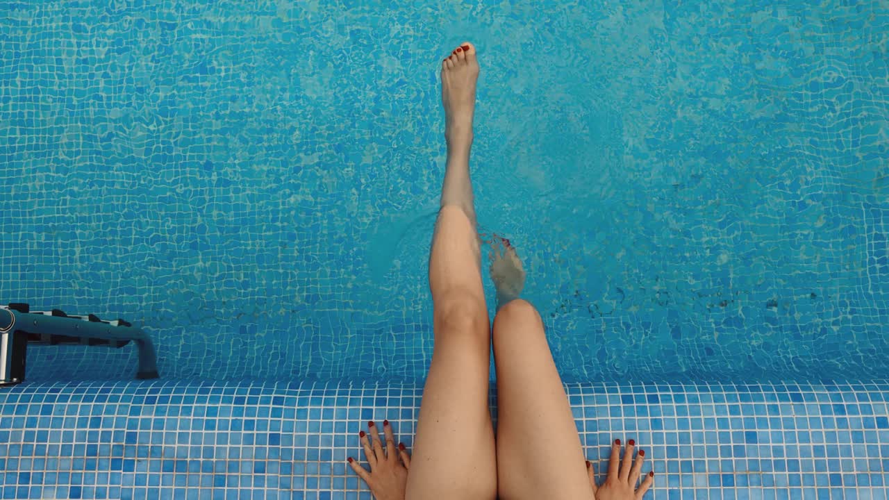 女子在清澈碧蓝的游泳池里荡着腿。暑假视频下载