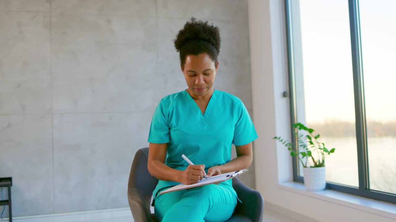 微笑的女护士坐着填写病人表格。视频下载