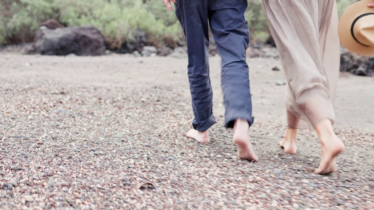 一对老年夫妇赤脚手牵着手走在沙滩上。视频下载