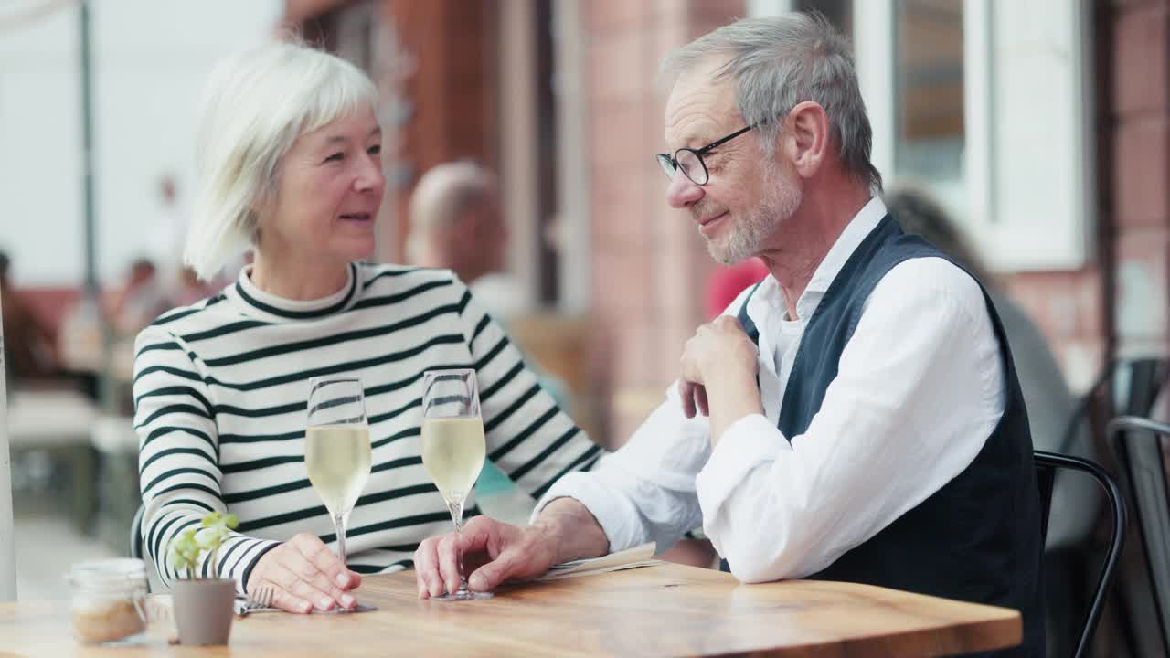 一对年长的情侣在户外酒吧享受着起泡的白葡萄酒，亲吻和享受。视频下载