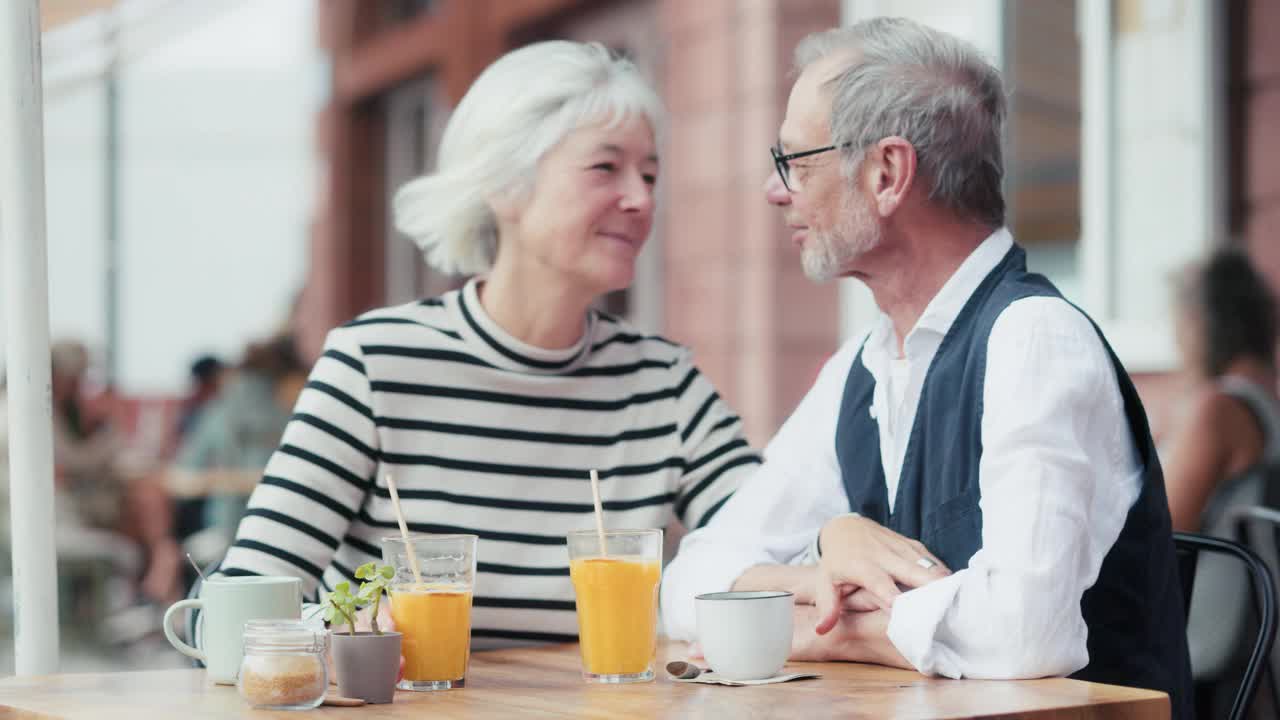 恋爱中的老年夫妇在有风的夏日早晨一起在户外吃早餐，在制定生活计划的同时玩得很开心。视频下载