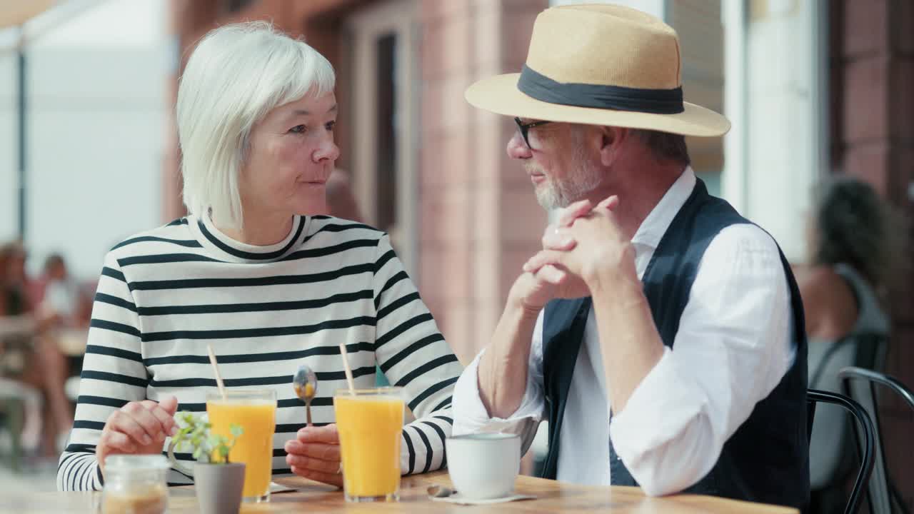 一对老年夫妇在有风的夏日里在户外吃早餐，谈论着未来。视频下载