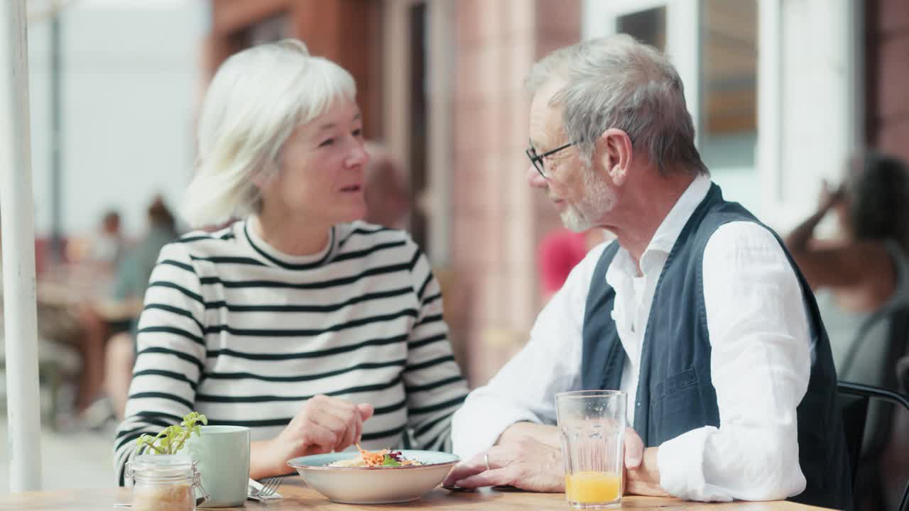一对老年夫妇在户外餐厅一起吃健康的素食午餐，边吃边聊天。视频下载