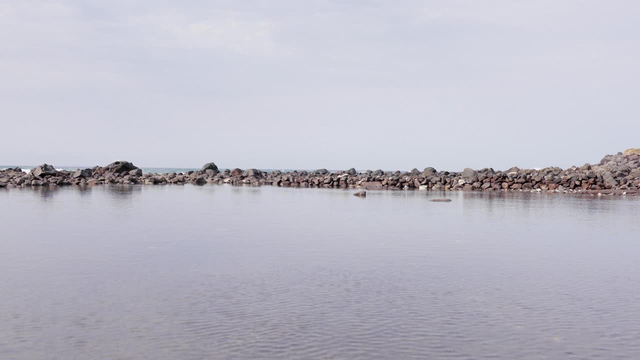 阳光明媚的假期里，一位70多岁的老人戴着遮阳帽在泻湖里涉水。视频下载