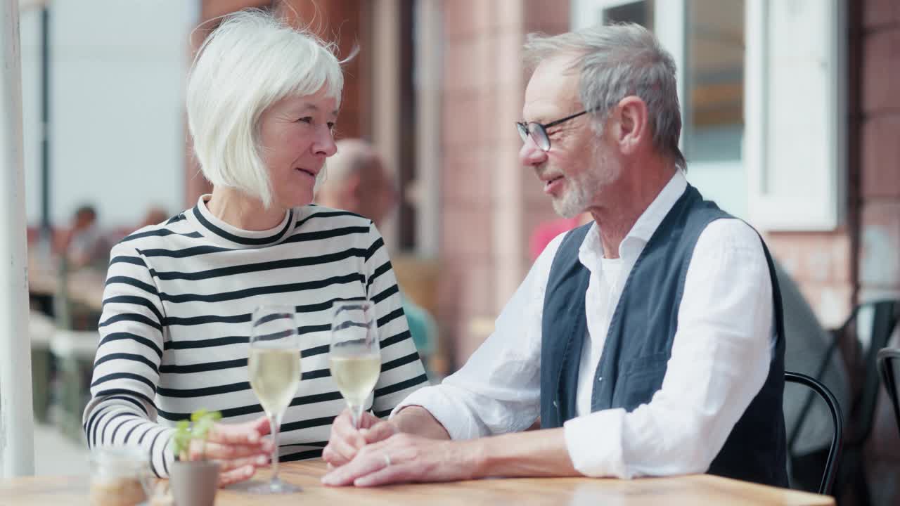 一对年长的情侣坐在户外餐厅里享受着起泡酒和自己，制定着宏伟的计划。视频下载