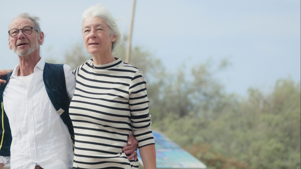 一对老年夫妇在阳光明媚的假期里手挽着手散步。视频下载