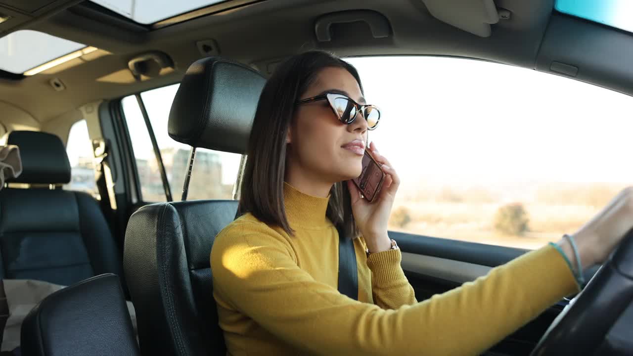 快乐的年轻女子一边在城市开车一边讲手机视频下载