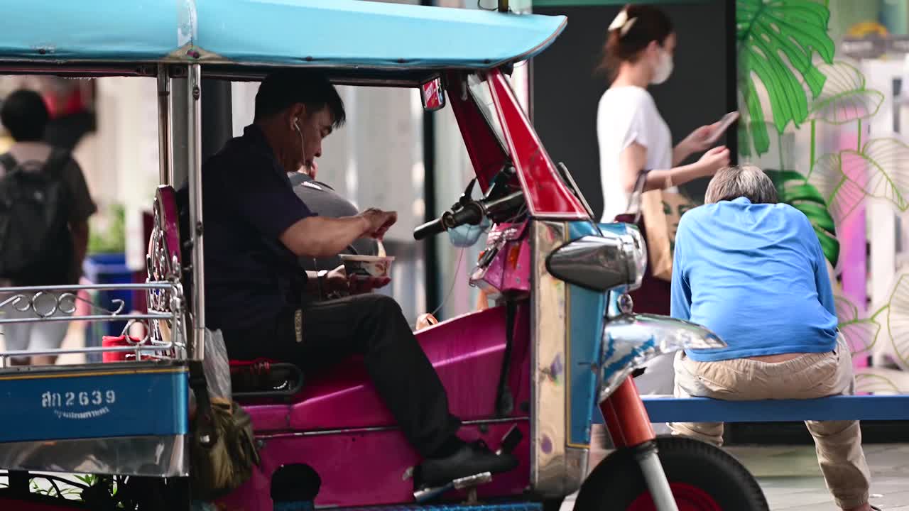 泰国曼谷，一名嘟嘟车司机坐在车里边等乘客边吃早餐视频下载