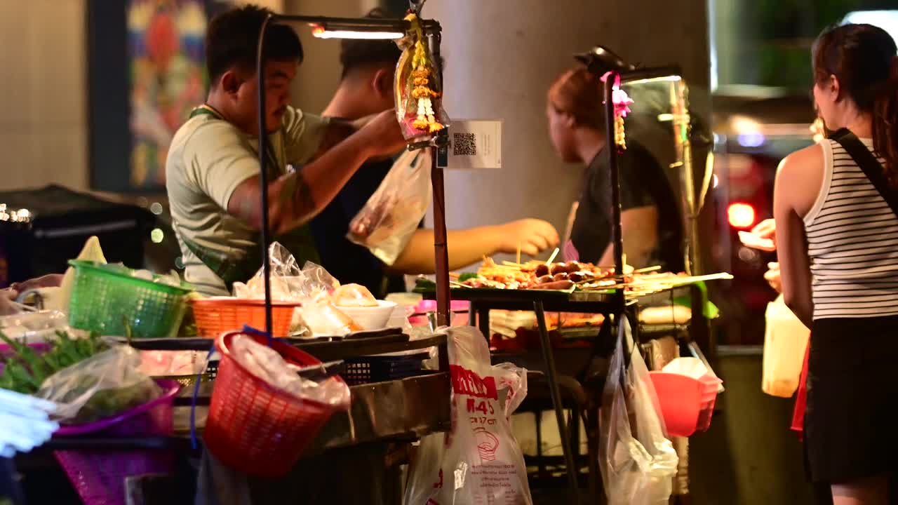 泰国曼谷，一名街头小贩在晚上的摊位上制作烤肉串视频下载