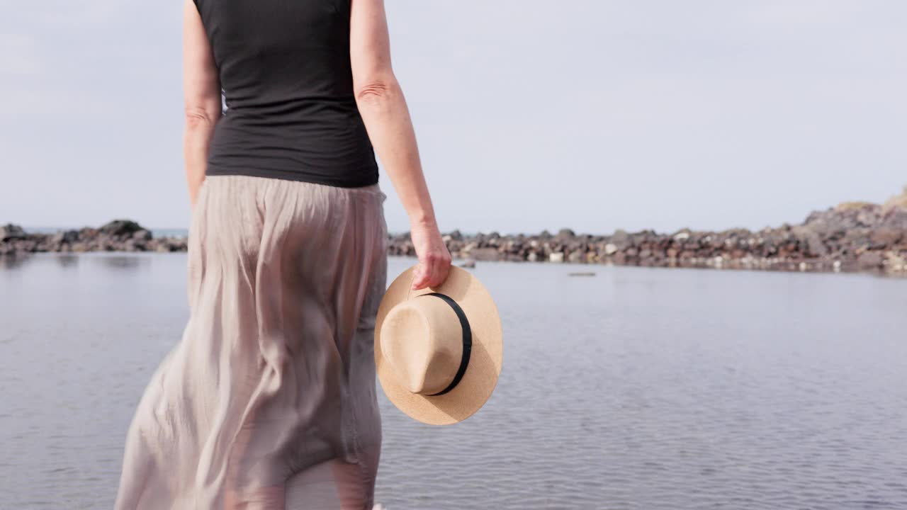 在阳光明媚的假期里，戴着太阳帽和裙子的快乐活跃的老年妇女在泻湖里涉水，享受风景。视频下载