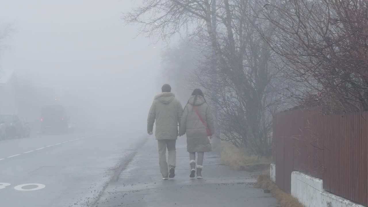 冰岛雷克雅未克，一对情侣手牵手漫步在雾蒙蒙的人行道上视频下载