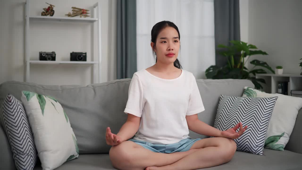 年轻女子在家里客厅的沙发上做瑜伽。视频下载