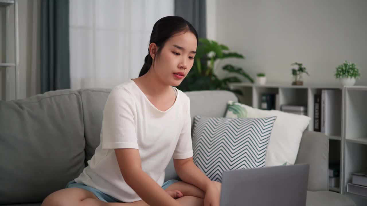 年轻女子在家里的客厅用笔记本电脑上的在线应用程序做瑜伽。视频下载