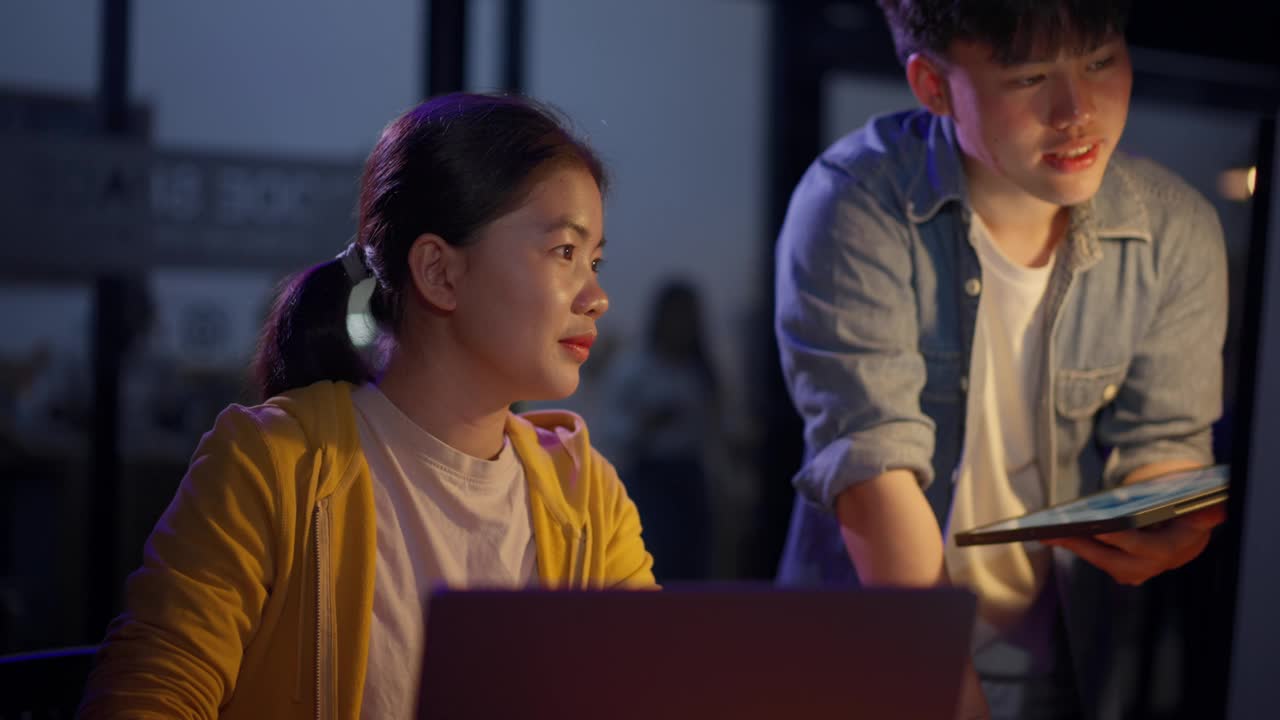 两个年轻的程序员在暖色调和冷色调的灯光下，在办公室里一起熬夜编写项目代码视频下载