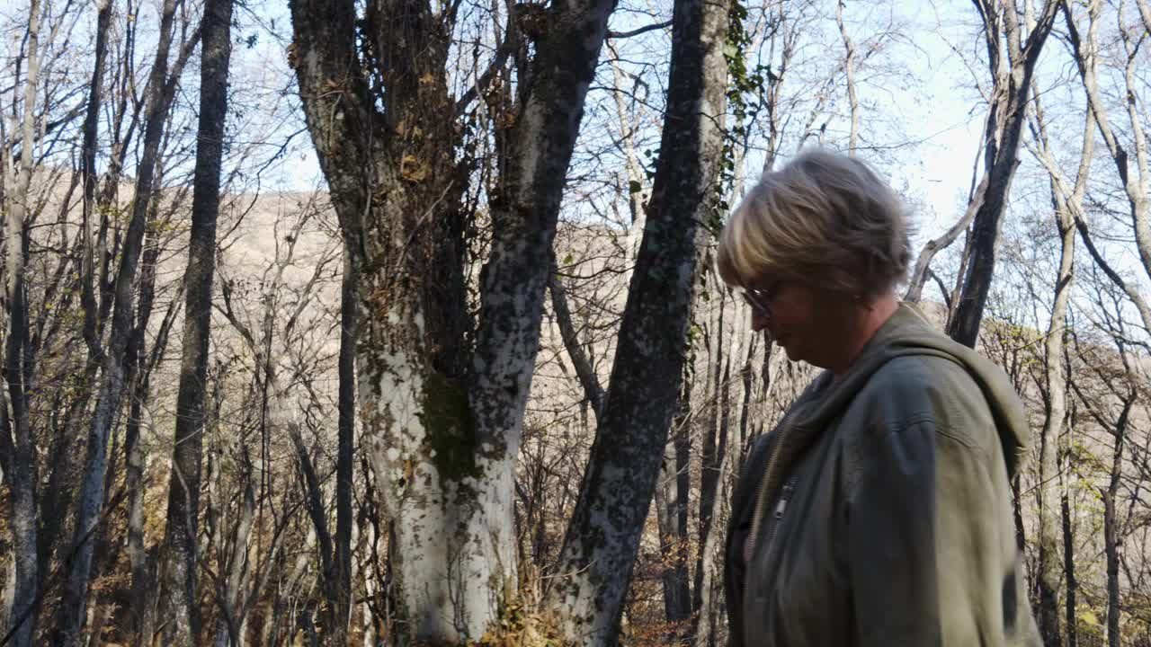 一位漂亮的老妇人在秋林的阳光下散步。金秋美景瑰丽。视频下载