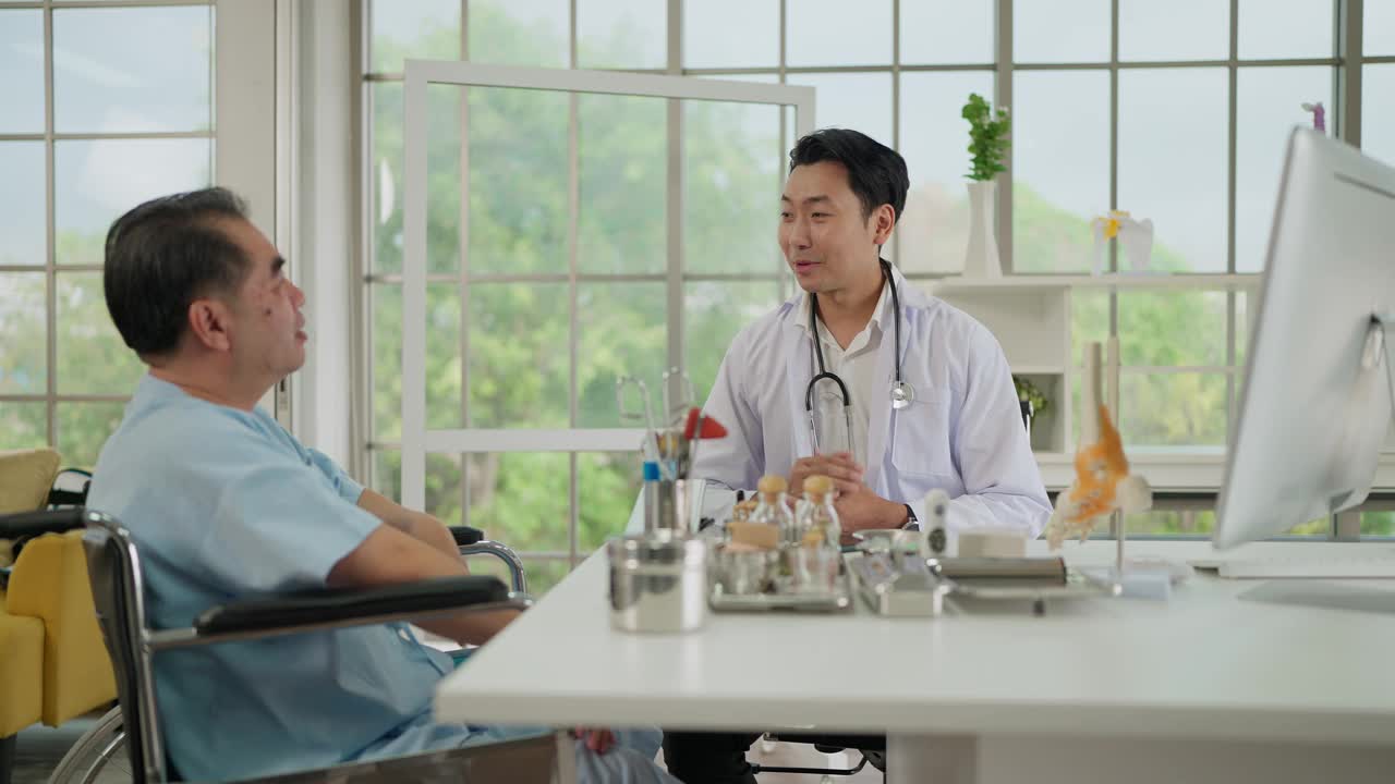 年轻的亚洲医生用电脑为一位老年男性病人讲解医疗报告，以诊断骨科和治疗关节疾病。理疗，保健理念视频下载