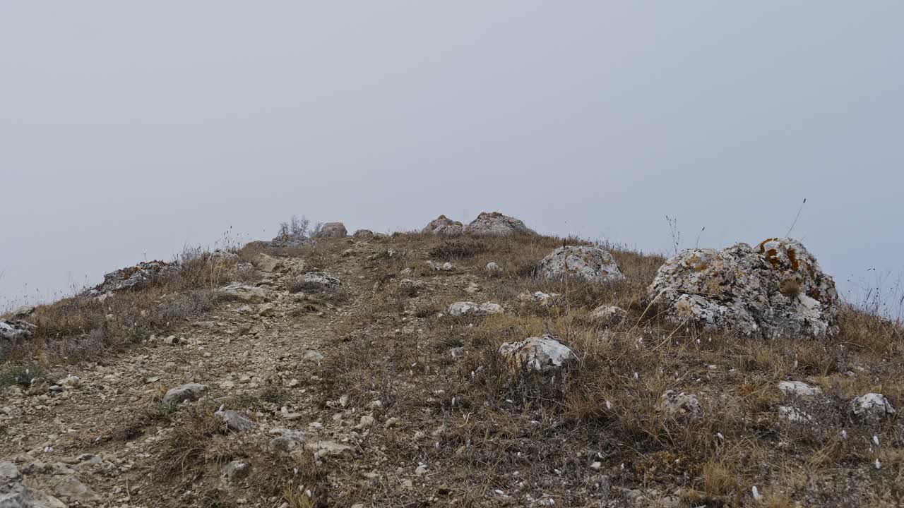 秋天走了。一个穿着舒适衣服的人爬上一条布满岩石的小路，进入浓雾。视频下载